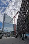 Rød tårnkran mellom moderne høyhus under en skyet himmel i et bysentrum.