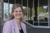 Smilende kvinne i lys blazer står foran en moderne bygning med glassvegger.