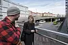 To personer står ved et rekkverk på en bro med vei og biler under, omgitt av bybygninger.