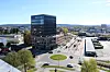 Rundkjøring foran et moderne kontorbygg med biler, parkeringsplasser og bylandskap.