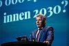 Bjørnar Skjæran står ved talerstol med vannkaraffel foran blå konferansebakgrunn.