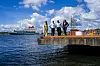 Fire politikere står på en brygge på Sukkerbiten i Oslo med fjorden og skip i bakgrunnen.