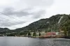 Nore I kraftverk ved Rødbergdammen med lav vannstand, fjell, skog og overskyet himmel.