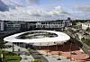 Ovalt hvitt tak over en moderne byplass med bygninger, stier og trær.