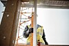 Bygningsarbeider i refleksvest holder et måleverktøy ved en delvis oppført konstruksjon.