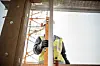 Bygningsarbeider i refleksvest holder et måleverktøy ved en delvis oppført konstruksjon.
