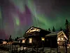 Nordlys i grønt og lilla over en opplyst hytte ved Sjusjøen om kvelden.