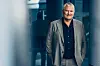 Per-Arne står i en moderne korridor iført grå dressjakke og mørk skjorte.