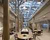Lyst atrium med restaurantbord, stoler, søyler og glasstak.