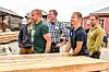 Gruppe mennesker står ved trelast på et utendørs arbeidsområde.