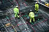 Tre arbeidere i neongrønne klær arbeider på et armeringsdekke sett ovenfra.