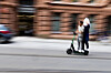 To personer på én elsparkesykkel passerer en bygning i Oslo.