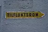 Gult skilt med teksten «TILFLUKTSROM» og pil mot høyre på en blågrå vegg.