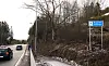 Blått skilt for Øygarden kommune langs en vei med biler og skog i vinterlandskap.